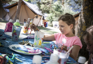 A girl paints crafts outdoors at a table at Huttopia Bourg Saint-Maurice in Auvergne-Rhône-Alpes, France.