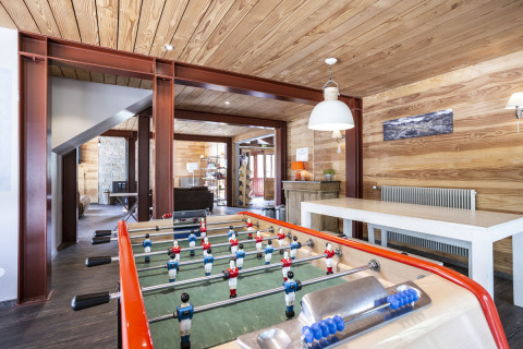 Sala de juegos con futbolín, paredes de madera y muebles modernos en Huttopia Bourg Saint-Maurice.