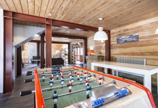 Spelkamer met tafelvoetbal, houten wanden en modern meubilair in Huttopia Bourg Saint-Maurice vakantiepark.