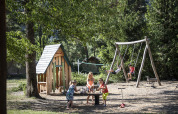 Children playing on a playground with swings and playhouse at Huttopia Bourg Saint-Maurice, France.