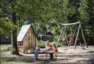 Kinderen spelen op een speeltuin met schommels en speelhuis bij Huttopia Bourg Saint-Maurice, Frankrijk.