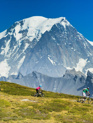 Ciclistas de montaña recorren senderos cerca de Bourg-Saint-Maurice con los Alpes franceses de fondo nevado.