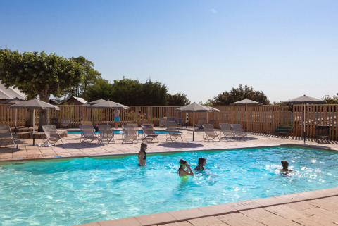 Piscina exterior en Huttopia Meursault con niños jugando y numerosas tumbonas y sombrillas alrededor.
