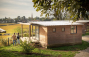 Paar steht vor einer Holzhütte im Chalet Evasion Vista Vue Vignes, Huttopia Meursault, Frankreich.