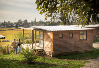 Pareja disfruta de la vista frente a una cabaña de madera en Chalet Evasion Vista Vue Vignes, Huttopia Meursault, Francia.