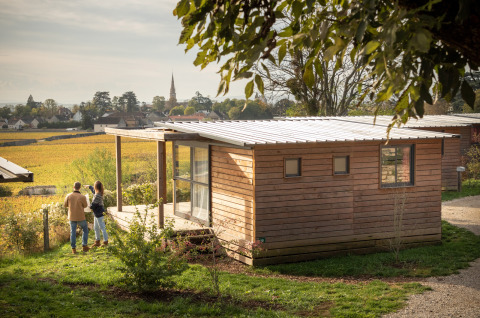 Couple enjoying the view in front of a wooden cabin at Chalet Evasion Vista Vue Vignes, Huttopia Meursault, France.