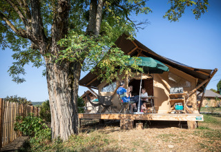 Familie nyder glamping foran et stort telt under et træ i Huttopia Meursault, Bourgogne-Franche-Comté.