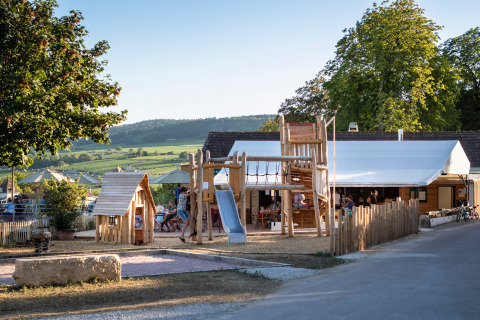 Parque infantil de madera en Huttopia Meursault, rodeado de viñedos y colinas en Bourgogne, Francia.