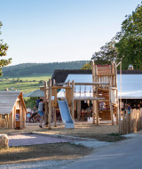 Parque infantil de madera en Huttopia Meursault, rodeado de viñedos y colinas en Bourgogne, Francia.