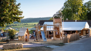 Parque infantil de madera en Huttopia Meursault, rodeado de viñedos y colinas en Bourgogne, Francia.