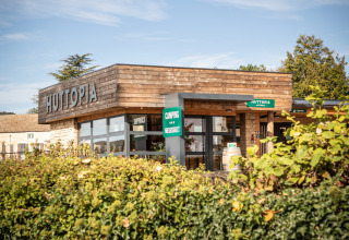 Ingang van vakantiepark Huttopia Meursault in Bourgogne-Franche-Comté, Frankrijk, met modern houten gebouw.