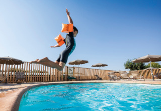 Kindje met zwembandjes springt in het zwembad op Huttopia Meursault vakantiepark onder blauwe lucht.