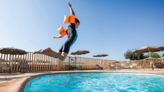 Niño con flotadores salta a la piscina en Huttopia Meursault, parque vacacional bajo cielo soleado.