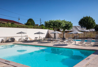 Udendørs swimmingpool med liggestole og parasoller på Huttopia Meursault i Bourgogne-Franche-Comté, Frankrig.