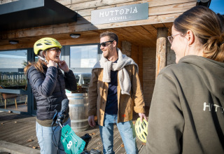 Tre personer smiler foran Huttopia Meursault i Bourgogne-Franche-Comté, Frankrig, hvoraf én har cykelhjelm på.