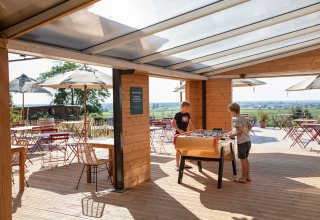 Niños juegan futbolín en una terraza cubierta en Huttopia Meursault, parque vacacional de Borgoña, Francia.