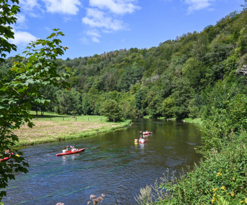 Personnes en kayak sur une rivière paisible entourée de collines vertes à Huttopia Vallée de la Semois, Namur.