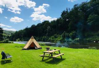 Zona de campamento con tienda, río y mesa de picnic en Huttopia Vallée de la Semois, Namur, Bélgica.