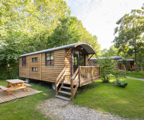 Holzhütte auf Rädern mit Veranda und Picknicktisch in der Natur im Huttopia Vallée de la Semois, Belgien.
