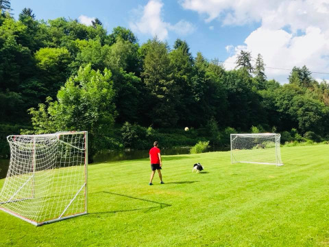 Hombre y perro juegan fútbol en campo verde con dos porterías en Huttopia Vallée de la Semois, Namur, Bélgica.
