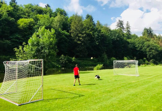 Uomo e cane giocano a calcio su prato verde con due porte a Huttopia Vallée de la Semois, Namur, Belgio.