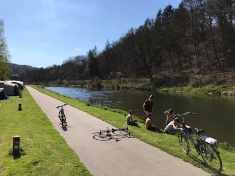 Persone rilassate vicino al fiume con biciclette e tende a Huttopia Vallée de la Semois, Namur, Belgio.