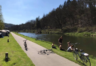 Personas descansan junto al río con bicicletas y tiendas en Huttopia Vallée de la Semois, Namur, Bélgica.