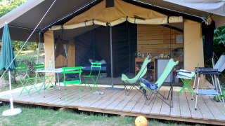 Tenda safari Toile&Bois Sweet con terrazza in legno, sedie verdi, cucina visibile e area relax.
