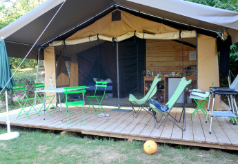 Safari telt Toile&Bois Sweet med grønne stole, træterrasse, og synligt køkken og soveområde.