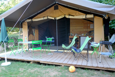 Tente safari Toile&Bois Sweet avec terrasse en bois, chaises vertes, coin cuisine et espace détente.
