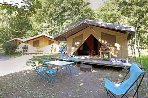 Safari tent Toile&Bois Sweet bij Huttopia Royat in Frankrijk met buitenstoelen, omgeven door groene bomen.