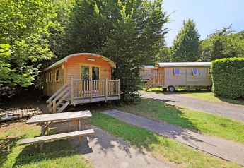 Zwei Holzwagen namens Gypsy Caravan bei Huttopia Royat in Frankreich, umgeben von Bäumen und Picknickbank.
