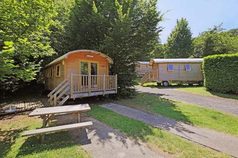 To træhusvogne kaldet Gypsy Caravan ved Huttopia Royat i Frankrig med grønne omgivelser og bænk.