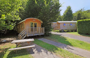 Two wooden Gypsy caravans at Huttopia Royat, France, surrounded by trees and a picnic bench in front.
