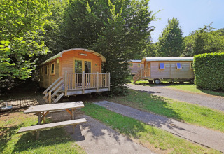 Two wooden Gypsy caravans at Huttopia Royat, France, surrounded by trees and a picnic bench in front.