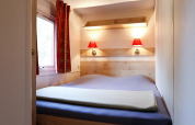 Dormitorio acogedor con cama doble, lámparas rojas, ventana y cortinas en una cabaña en Huttopia Royat, Francia.