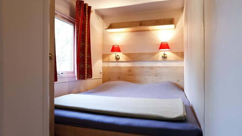 Dormitorio acogedor con cama doble, lámparas rojas, ventana y cortinas en una cabaña en Huttopia Royat, Francia.