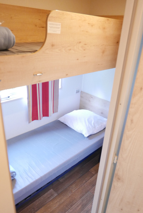 Køjeseng med træramme og enkeltseng i kabinen Gypsy caravan på Huttopia Royat, Frankrig.