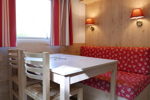 Hyggeligt spiseområde i Gypsy caravan på Huttopia Royat, Frankrig, med træbord, stole og rød sofa.