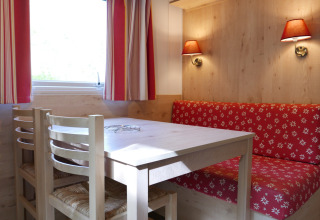 Coin repas chaleureux dans la roulotte à Huttopia Royat, France, avec table, chaises et banquette rouge.