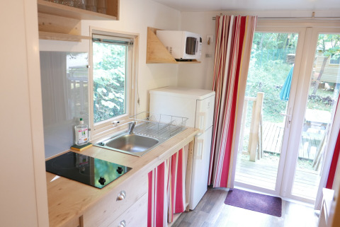 Pequeña cocina en caravana Gypsy en Huttopia Royat, Francia, con nevera, estufa, fregadero y terraza.