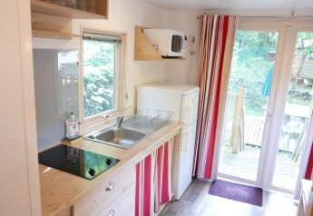 Pequeña cocina en caravana Gypsy en Huttopia Royat, Francia, con nevera, estufa, fregadero y terraza.
