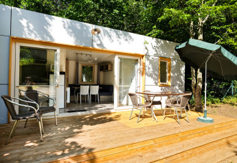 Mobile Home Vancouver: Holzterrasse mit Sitzgruppe und Sonnenschirm im Grünen vor einem modernen Modulhaus.