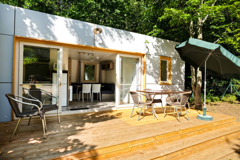 Mobile home Vancouver: houten terras met stoelen, tafel en parasol bij een modern huisje in het bosrijk groen.