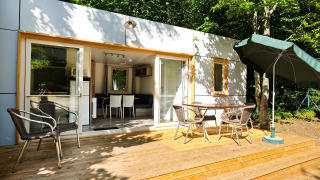 Casa móvil Vancouver: terraza de madera con mesa, sillas y sombrilla, rodeada de bosque verde y naturaleza.