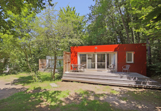 Rotes Mobilheim mit Holzterrasse inmitten von Bäumen im Huttopia Royat, Frankreich, im Sommer.