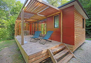 Stacaravan Vancouver bij Huttopia Royat in Frankrijk met houten terras, ligzetels en groene bosomgeving.