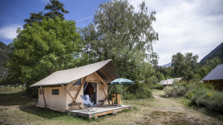 Safari Trappeur-tent met stoelen en parasol op houten terras, omringd door bomen en natuurgebied.