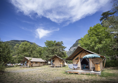 Trappeur safari tents at Huttopia Bourg Saint-Maurice, France, with mountains and green trees around them.