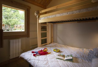 Udsigt over et hyggeligt værelse med køjesenge og vindue i Montana Chalet på Huttopia Bourg Saint-Maurice, Frankrig.